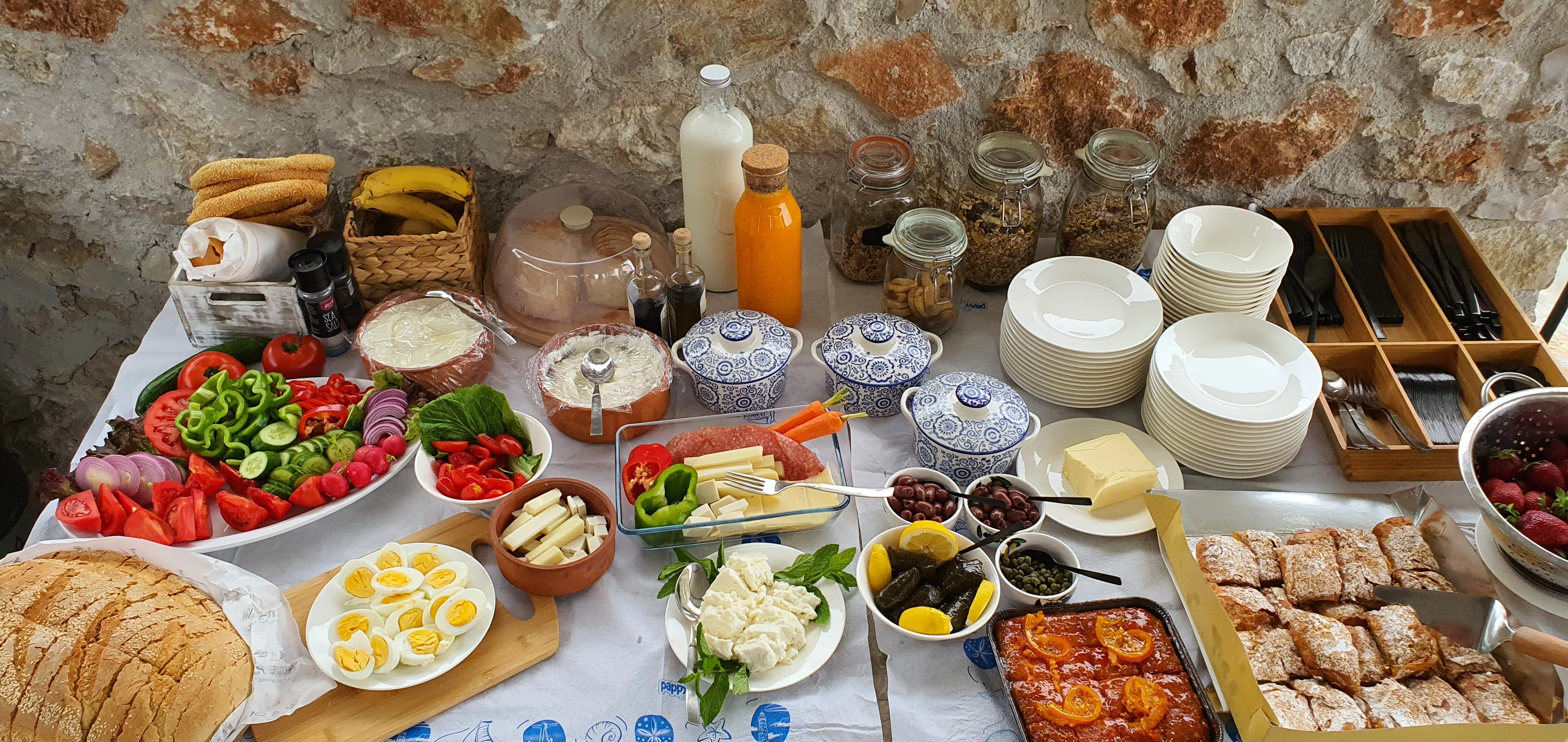 Breakfast spread with local produce, eggs, pastries and preserves laid on a long table against a stone wall
