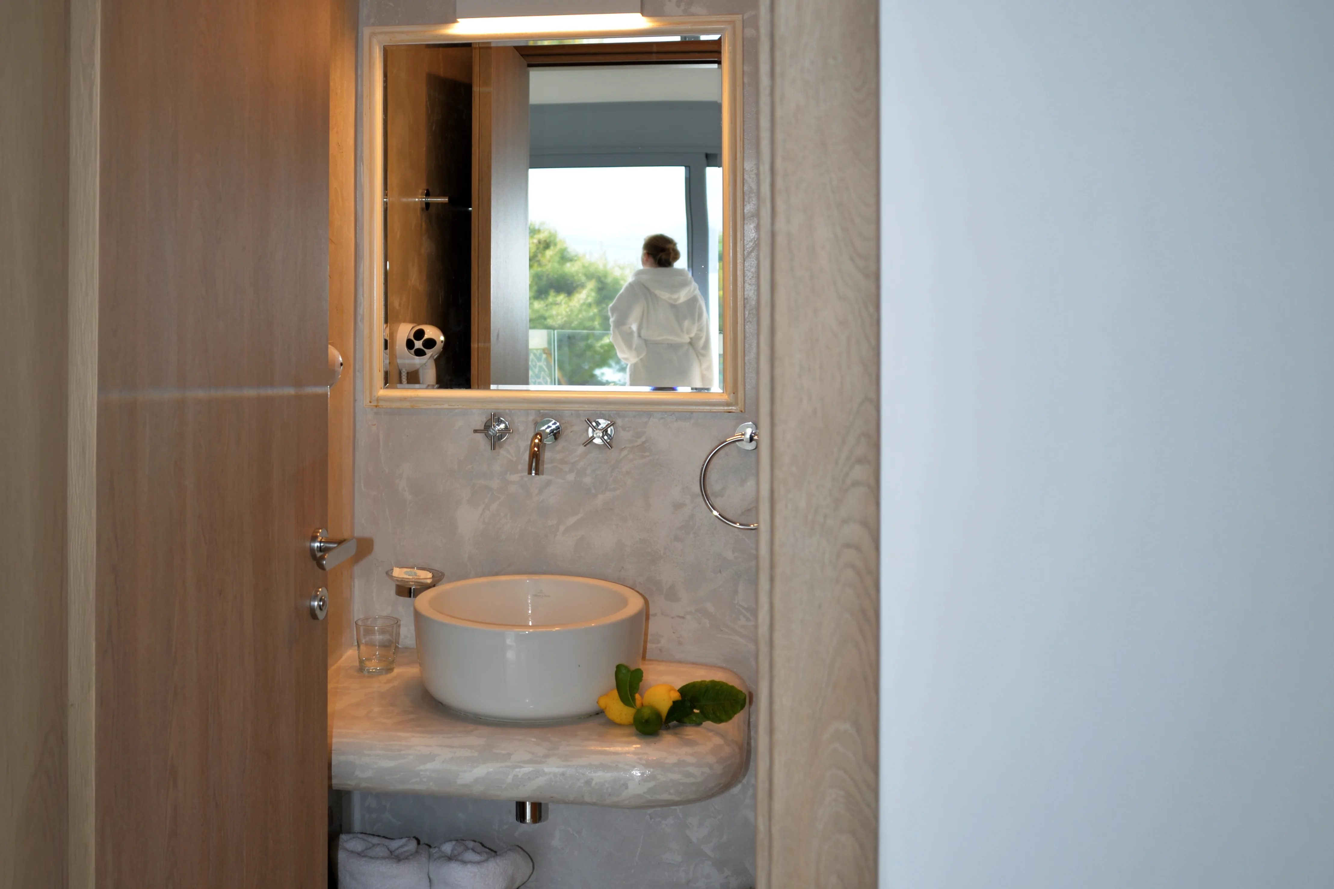 Bathroom with round basin and mirror reflecting a guest in a robe