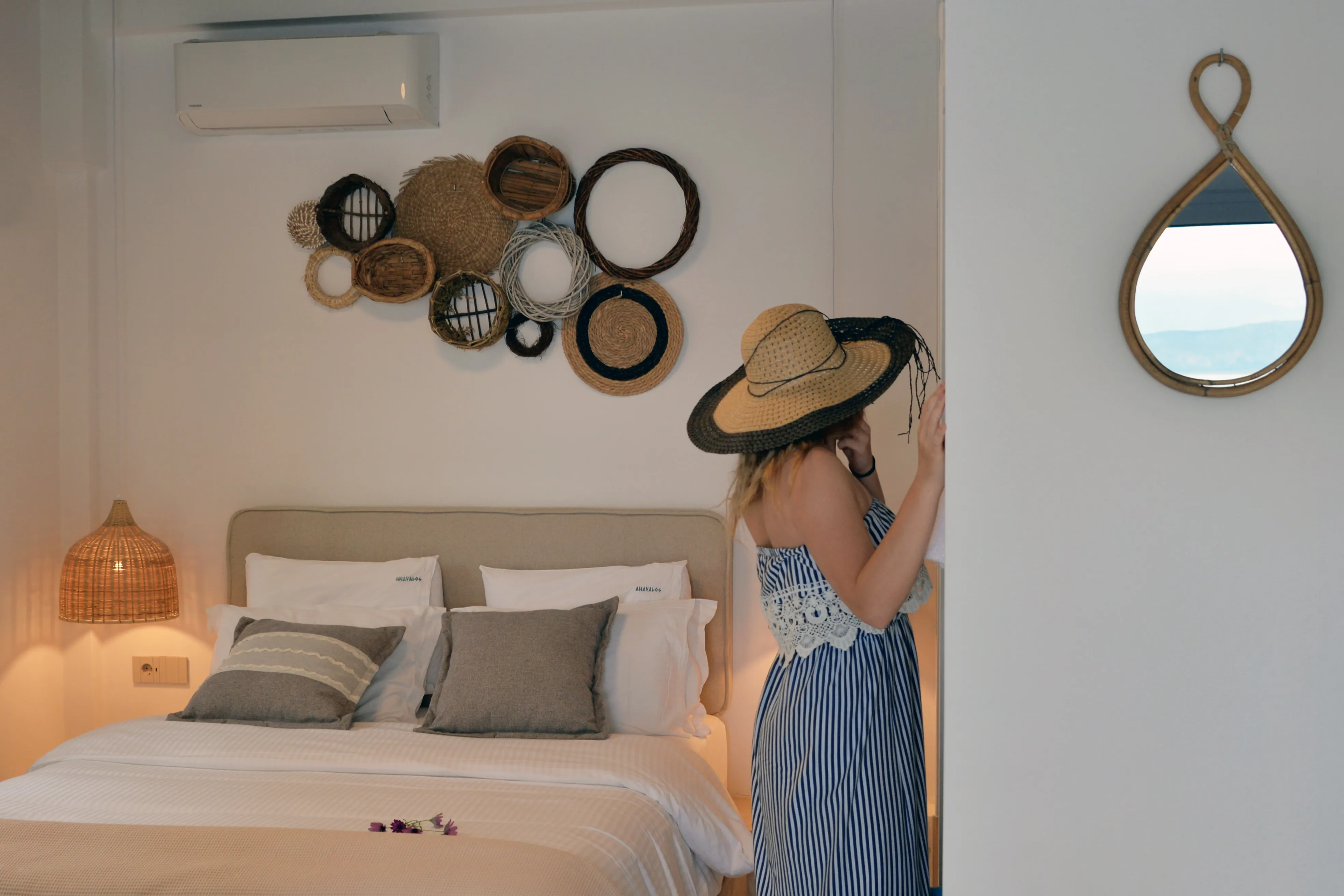 Notos bedroom with woven wall baskets and a guest trying on a sun hat
