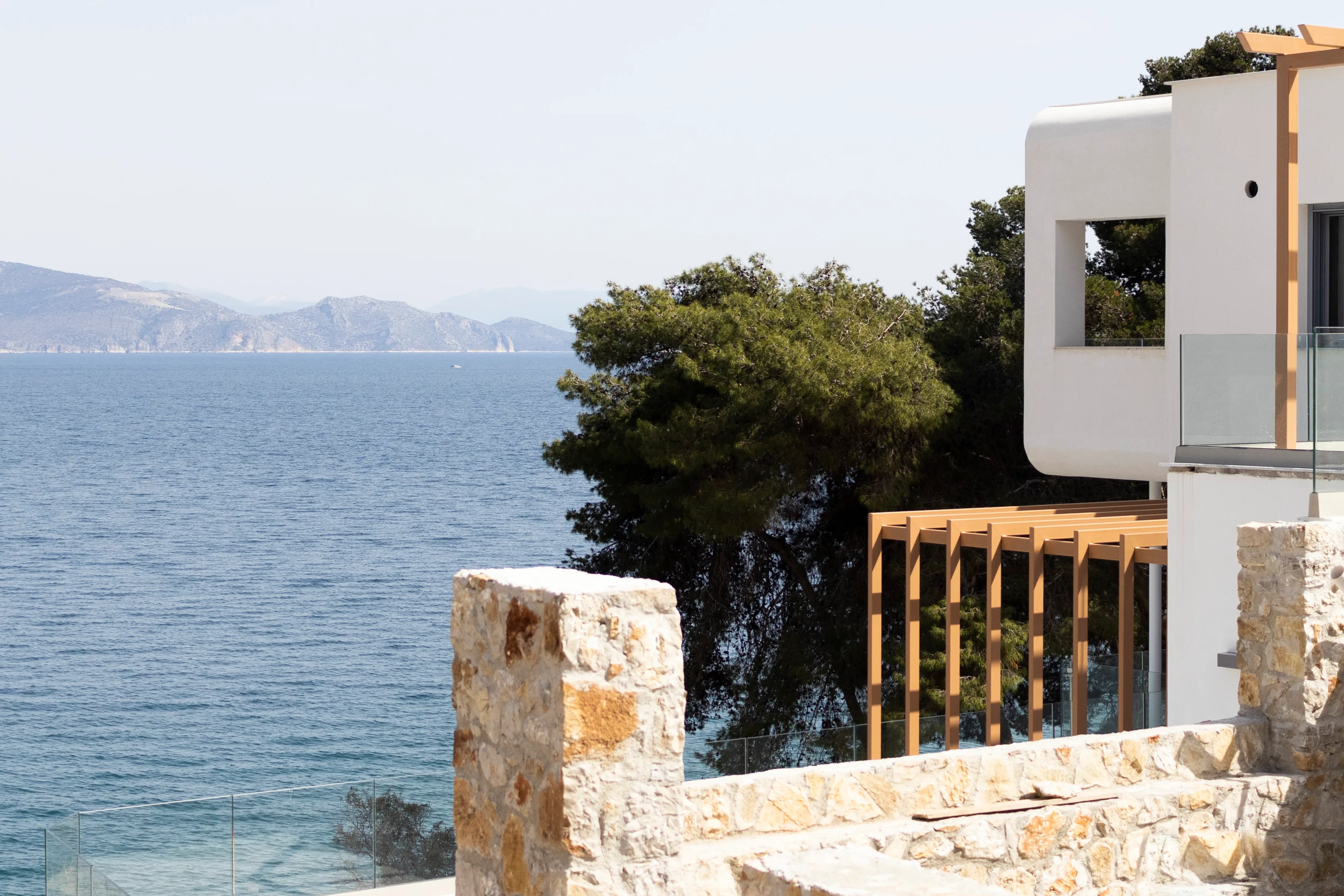 White curved architecture, timber pergola and stone wall above the sea
